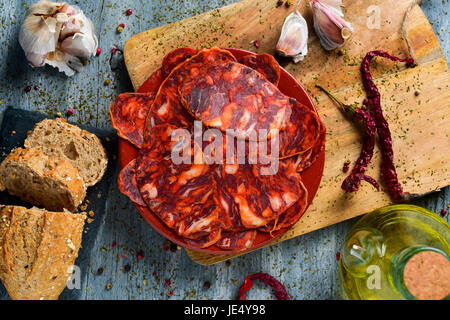 High-Angle Shot eines Steingut Platte mit einige Scheiben der spanischen Chorizo, Wurstwaren Wurst, einige Scheiben Brot, ein Glas Menage mit Olivenöl ein Stockfoto