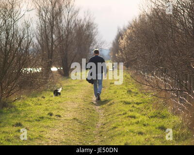 Ein Mann, der einen Hund entlang des Kanalufers in Sheerness, Kent, Großbritannien, spazieren geht. Stockfoto