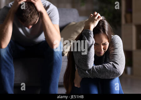 Traurig paar nach Streit oder Trennung sitzen auf einem Sofa im Wohnzimmer in einem Haus mit einem dunklen Hintergrund indoor Stockfoto