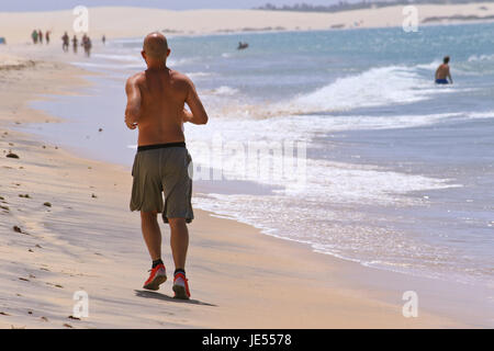 Sportlicher Mann läuft entlang des Strandes auf den Ozean für den perfekten Körper in Ordnung zu halten Stockfoto