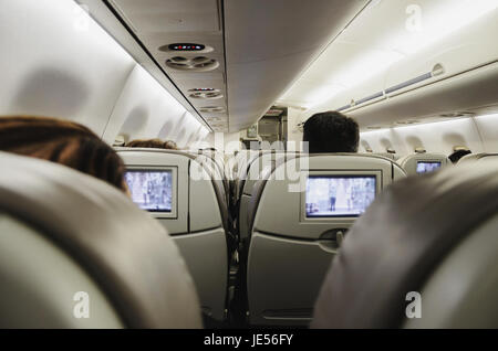 Menschen an Bord des Flugzeugs sitzen in ihren Sitzen vor dem Fernseher und wartet auf das Flugzeug abheben. Stockfoto