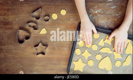 Draufsicht des Kindes mit rohen geformte Plätzchen auf Backpapier legen und Cookie Cutter auf Holztisch Stockfoto