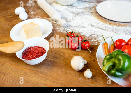 Teig auf hölzernen Tischplatte, verschiedene Pizza-Zutaten und Gemüse Stockfoto