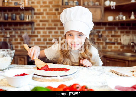 kleines Mädchen, Tomatensauce auf Pizzateig Stockfoto