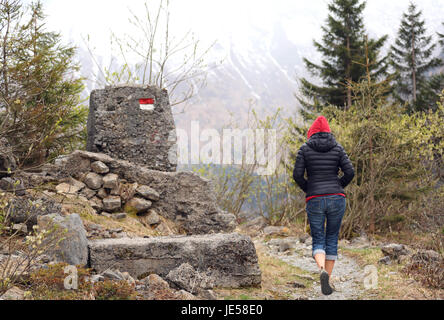 junge Frau mit roter Haube geht auf Bergpfad im winter Stockfoto