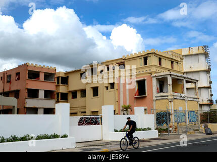 Ein Mann reitet auf seinem Fahrrad entlang einer Straße vor einige verfallenen Apartment-Gebäude in San Juan, Puerto Rico. Stockfoto