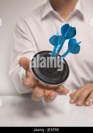 Mann Hand, die ein Ziel mit drei Darts schlagen die Mitte, blau und Beige Töne, Konzept-Bild zur Veranschaulichung des Marketing oder Business-Lösungen Stockfoto