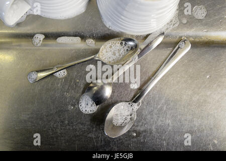 Teelöffel mit Seifenblasen und weiße Tassen auf Abtropffläche aus Edelstahl. Stockfoto