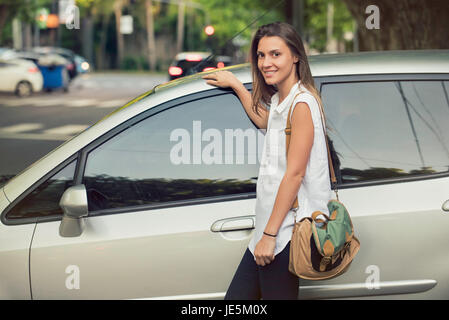 Junge Frau lehnt sich an Auto, Lächeln Stockfoto