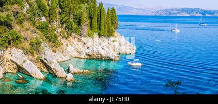 Felsenküste von Zypressen bedeckt und tourest Boote im azurblauen Wasser, in der Nähe von Kalami, Corfu Stockfoto