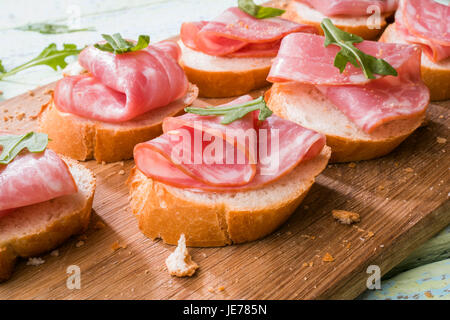 Foto von Brot mit Schinken und Grüns auf weißer Holztisch Stockfoto