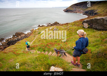 Ein Mann und eine Frau paar loslaufende Hunde entlang der Cornwall Coast Path zwischen Port Quin und Port Isaac in Cornwall, England Stockfoto