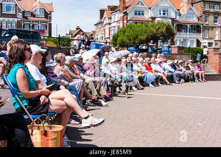 Reihe der Leute sitzen Liegestühle im Halbkreis beobachten (unseen) zeigen beim Musikpavillon in Broadstairs im Sommer. Strahlender Sonnenschein. Low Angle Sicht. Stockfoto