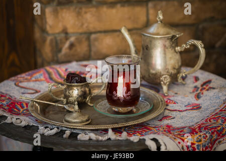 Tee-Set im orientalischen Stil in Birne geformt Glas mit Löffel und Vintage Wasserkocher und Termine Frucht auf silbernen Tablett auf silbernen Tablett gegen Mauer Stockfoto