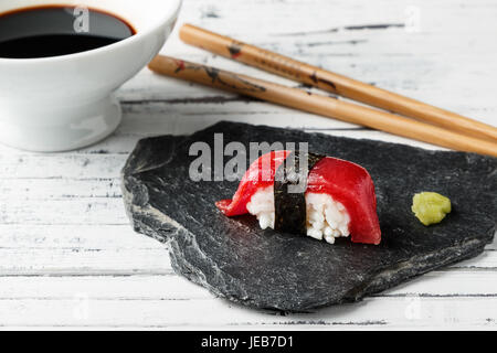 Roter Thunfisch Nigiri mit Nori-Algen und Wasabi paste auf Schiefer. Ess-Stäbchen und Schüssel mit Sojasauce im Hintergrund alte weiße Holz. Roher Fisch in Stockfoto