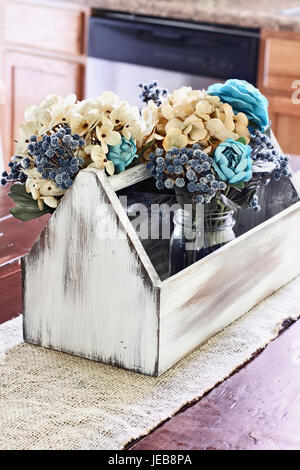 Innen rustikale Bauernhaus Küchentisch mit alten Vintage Holz Toolbox mit faux Blumen in ein Einmachglas. Extrem geringe Schärfentiefe. Stockfoto