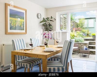 Ein Esstisch für eine Mahlzeit & Stühle in einem kleinen frisches Gefühl Esszimmer mit Glastüren, die auf einen kleinen Garten im Innenhof Stockfoto