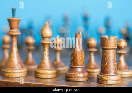 Alte hölzerne Schachfiguren auf einem alten Schachbrett. Auf einem blauen Hintergrund. Stockfoto