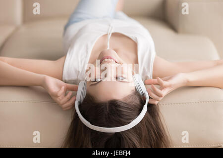 Junge Frau auf Sofa liegend mit Kopfhörer auf Kopf Stockfoto