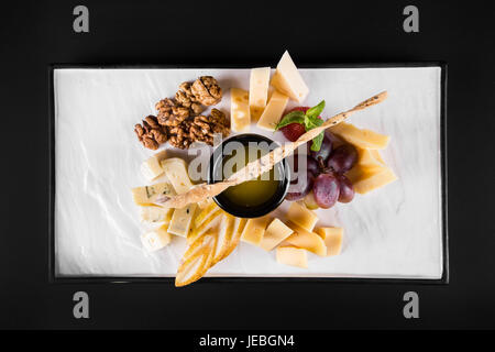 Einen großen Teller mit einer großen Auswahl an Snacks wie Käse, Walnüsse, Trauben, Cracker auf dunklem Hintergrund. Ansicht von oben Stockfoto