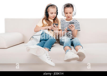 Niedlichen Mädchen mit Smartphones, hören Musik auf couch Stockfoto