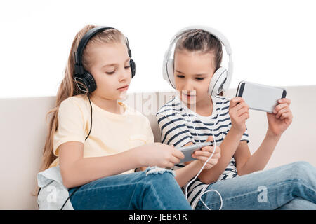 Niedlichen Mädchen mit Smartphones, hören Musik auf couch Stockfoto