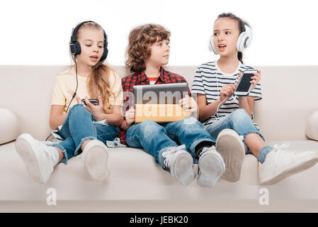 Cute kids mit digitalen Geräten, Musik hören auf couch Stockfoto