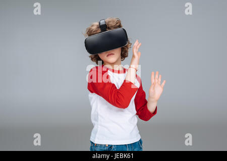 Kleiner Junge mit virtual-Reality-Kopfhörer isoliert auf grau Stockfoto