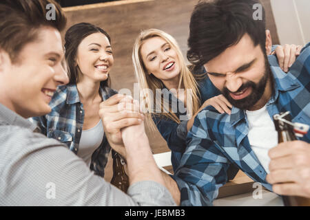 Zwei Männer mit den Händen umklammert im Armdrücken Herausforderung während Frauen an Hintergrund anzuschauen Stockfoto