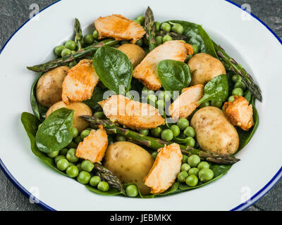 Hähnchen-Salat mit Spargel Erbsen Spinat und Kartoffeln vor schwarzem Hintergrund Stockfoto