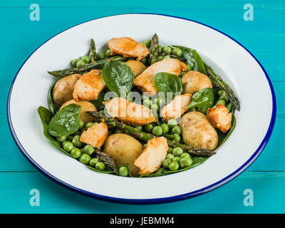 Hähnchen-Salat mit Spargel Erbsen Spinat und Kartoffeln auf blauem Grund Stockfoto