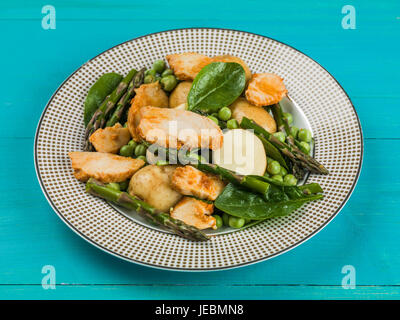 Hähnchen-Salat mit Spargel Erbsen Spinat und Salzkartoffeln auf blauem Grund Stockfoto