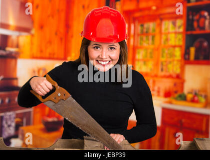 Schöne junge Frau Zimmermann Schneiden von Holz mit einer Säge lächelnd Stockfoto