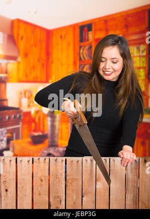 Wunderschöne lächelnde junge Frau Schneiden von Holz mit einer Säge für ein Projekt Stockfoto