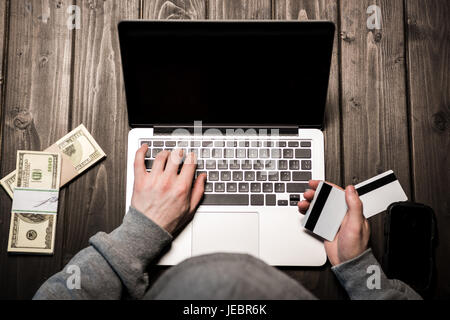 Schuss von jungen Hacker in Hoodie hält Kreditkarte und mit Laptop zugeschnitten Stockfoto