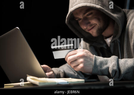 Junge Hacker in Hoodie hält Kreditkarte und mit laptop Stockfoto
