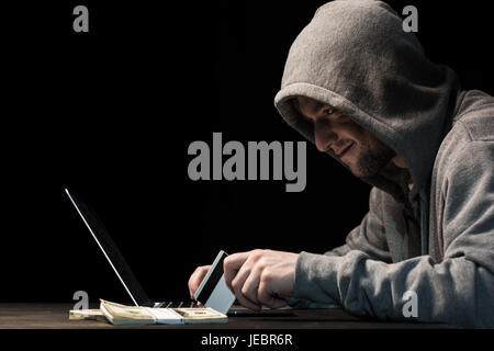 Junge Hacker in Hoodie hält Kreditkarte und mit laptop Stockfoto