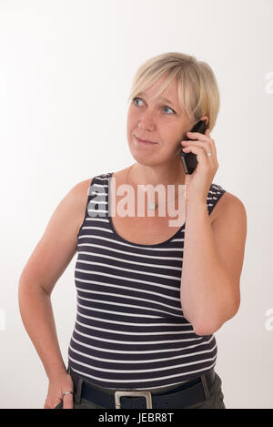 Porträt von einer attraktiven Blondine Rothaarige Mitte Alter Europäerin tragen Blau gestreiftes Top Schauspiel mit Mobiltelefon - Studio gedreht auf weißem Hintergrund. Stockfoto