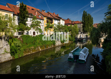 Historische Häuser auf den Efeu bedeckt Hribar Quay Ufer der Ljubljanica Flusses Kanal Wasserstraße mit Ausflugsschiff in der alten Stadt von Ljubljana Slowenien Stockfoto