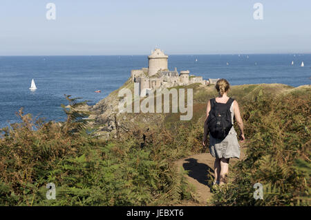 Europa, Frankreich, Bretagne, Cote D' Emeraude, Cap Frehel, Frau auf Fußweg, im Hintergrund die Festung la Schlossbar Stockfoto