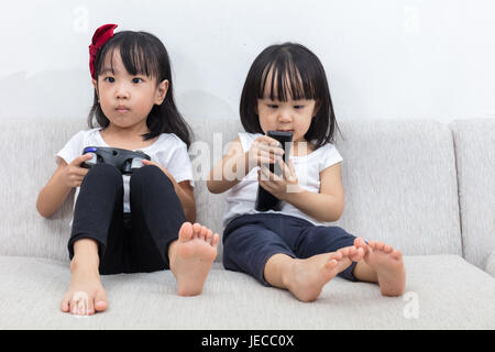 Asiatische chinesische kleinen Schwestern spielen TV auf dem Sofa im Wohnzimmer zu Hause. Stockfoto