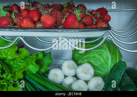 Tablett mit Erdbeeren, Salat, Frühlingszwiebeln, Knoblauch, Kohl und Gurken in Kühlschrank Regalen. Unscharfen Hintergrund. Stockfoto