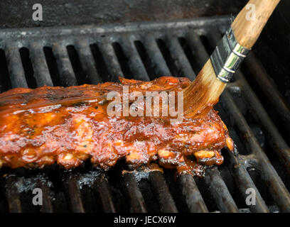 Bürste slathering BBQ-Sauce auf einige zarte Baby Back Ribs. Geringe Schärfentiefe - Schwerpunkt am Ende des Pinsels. Stockfoto