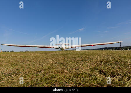 Ein Segelflugzeug mit einer Schutzhülle auf einem grasbewachsenen Flughafen an einem sonnigen Tag geparkt. Stockfoto