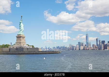 Statue von Liberty Island und New York City Skyline an einem sonnigen Tag, weiße Wolken Stockfoto