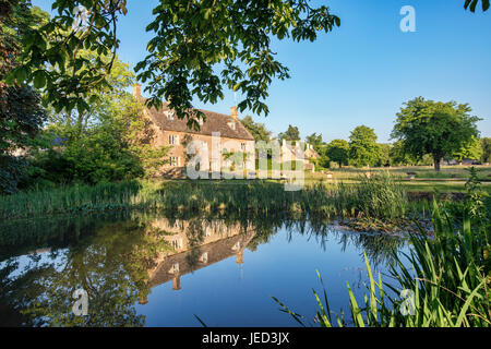 Wyck Rissington Dorfteich und Reflexionen in den späten Abend Juni Sonnenschein. Cotswolds, Gloucestershire, England Stockfoto