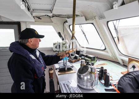 Älterer mann Pilotierung Boot, Innenraum des Schiffs Brücke, Mann in der Rettungsweste durch Fenster mit Blick auf das Meer. Von der Seite. Stockfoto