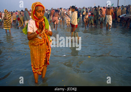 Indien, Westbengalen, Sagar, Sagar Festival Pilger Seniorin tragen rote und gelbe Sari beten im Wasser im Vordergrund. Stockfoto