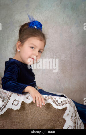 wunderschönes kleines Mädchen Prinzessin im blauen Kleid auf weißen Stuhl sitzen und Lächeln Stockfoto