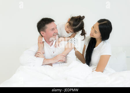 Familie mit schönen Mutter gut aussehend Vater mit niedlichen kleinen Tochter sprechen und Lächeln während Sie verbringen Zeit zusammen im Bett. Glückliche Familie c Stockfoto